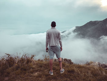 Rear view of man standing on mountain against sky