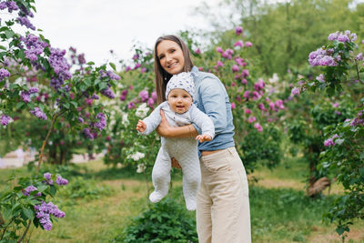 Young mother holds her baby son in her arms in a spring blooming lilac park