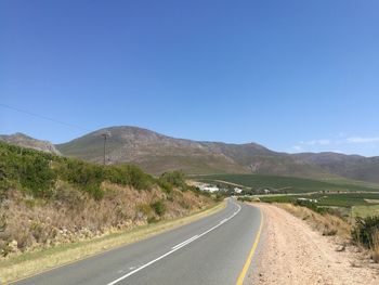 Empty road along landscape against clear blue sky