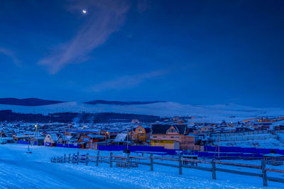 Scenic view of snow covered buildings against blue sky