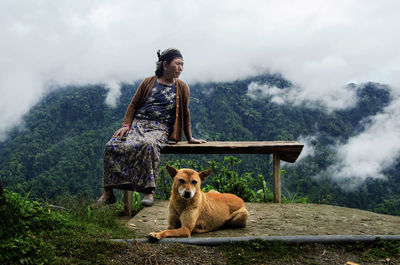 Senior woman sitting on table by dog on mountain