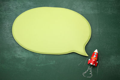 Directly above shot of blank speech bubble with toy rocket on blackboard