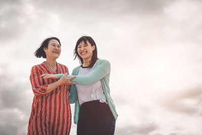 Happy mother and daughter standing against sky