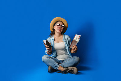 Young woman wearing hat sitting against blue wall