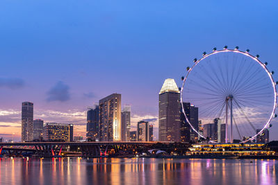 Illuminated ferris wheel in city against sky at dusk