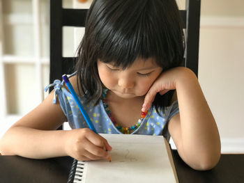 Portrait of cute girl drawing in book at home