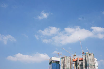 Low angle view of crane and buildings against blue sky