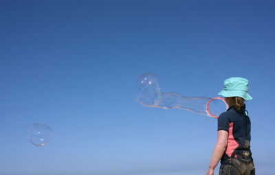 Side view of woman holding bubbles against clear blue sky