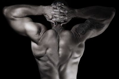 Rear view of shirtless man flexing muscles against black background