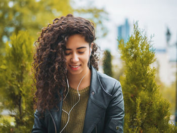 Young woman listening to music against trees