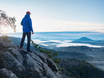 Man on mountain peak look on mountain valley in early autumn. landscape with traveler, foggy hills