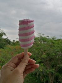 Hand holding ice cream cone against sky