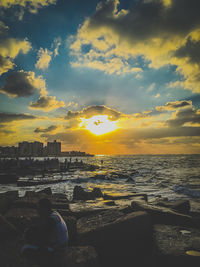 Rear view of man standing at beach against sky during sunset