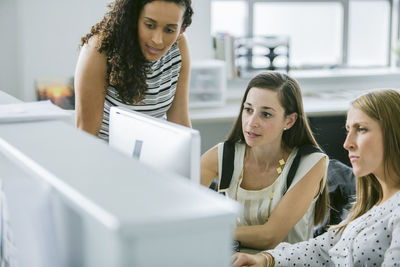 Female colleagues looking at desktop computer while working at desk in office