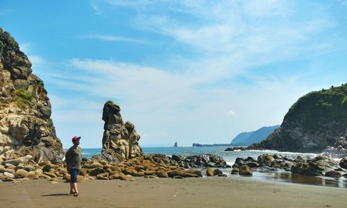 Rear view of woman standing on rocks at beach