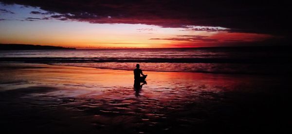 Silhouette person standing on beach during sunset