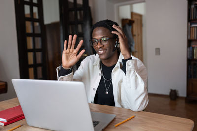 Smiling optimistic african american man waving hand having video call in laptop with friends