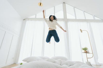 Low angle view of woman jumping on bed at home
