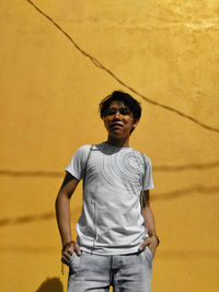 Portrait of young man standing against yellow wall