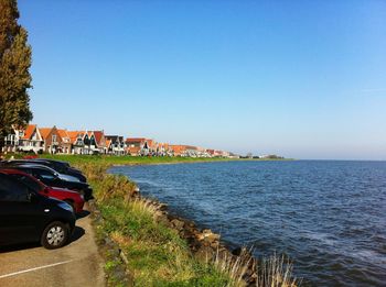 Cars parked by lake against clear blue sky