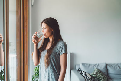 Young woman drinking wine while standing against white background