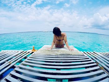 Rear view of woman sitting by swimming pool against sky