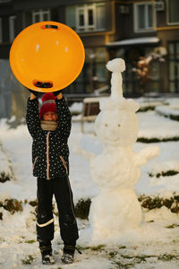 Winter portrait of a girl with a plastic sled sliding on a snowy slope and making a snowman