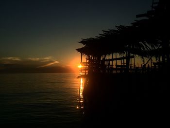 Silhouette palm trees by sea against sky during sunset