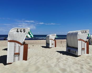 Hooded chairs on beach against blue sky