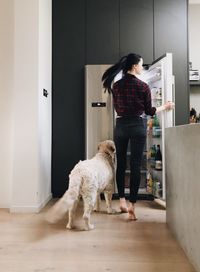 Rear view of woman opening fridge with dog in kitchen