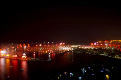 Illuminated city by river against sky at night