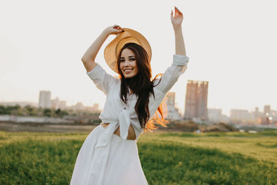 Portrait of smiling young woman standing on field against sky