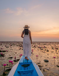 Rear view of woman standing at beach against sky during sunset