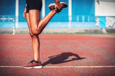 Low section of female athlete stretching leg on sports track