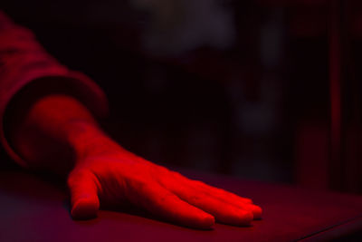 Red light falling on cropped hand at table