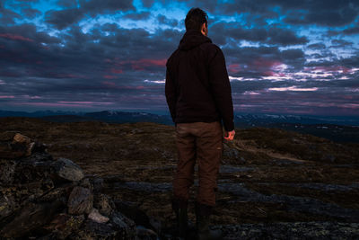 Rear view of man standing on rock against sky during sunset