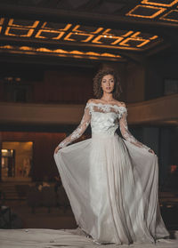 Portrait of beautiful woman holding wedding dress while standing in old building