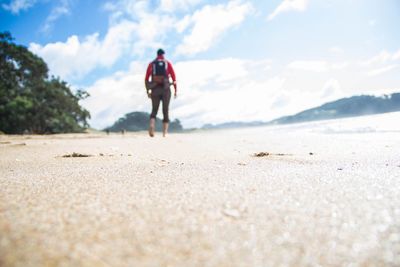 Rear view of woman walking on beach against sky