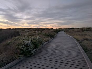 Boardwalk leading towards landscape against sky during sunset