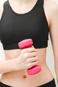 Young beautiful caucasian teen girl in a fitness suit holds pink dumbbell with one hand .