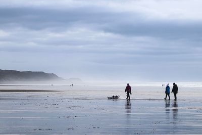 People walking on shore at beach against sky