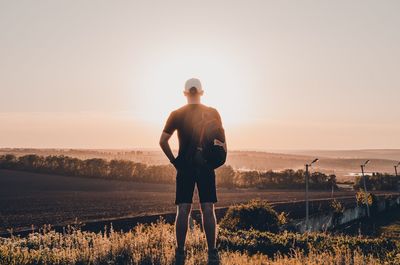 Rear view of man standing on field against sky during sunset