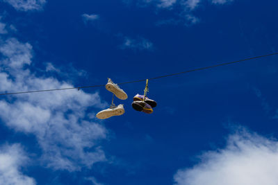 Low angle view of shoes hanging on rope against blue sky