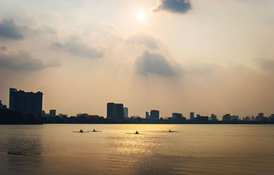 Silhouette buildings by sea against sky during sunset