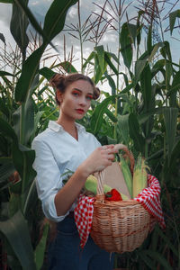 A beautiful girl with two bagels of hair in a cornfield. a basket with corn and a book