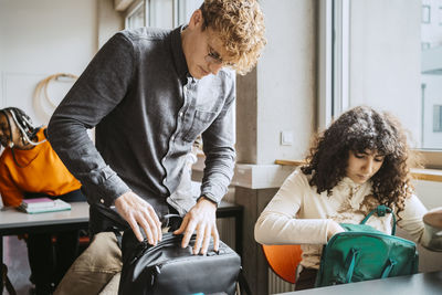 Young man and woman packing backpack in classroom at university