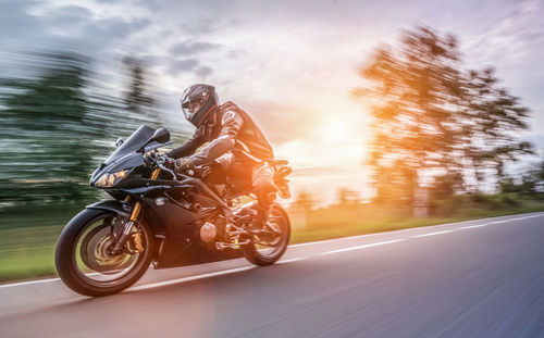 Blurred motion of man riding motorcycle on road against cloudy sky