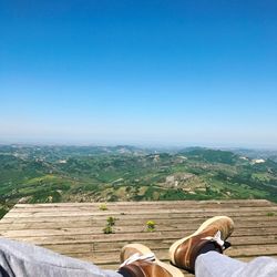 Low section of man relaxing on mountain against blue sky