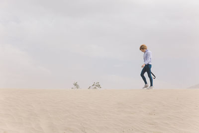 Man on sand dune in desert against sky