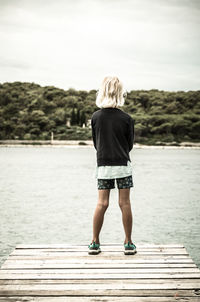 Rear view of girl standing on pier over lake against sky